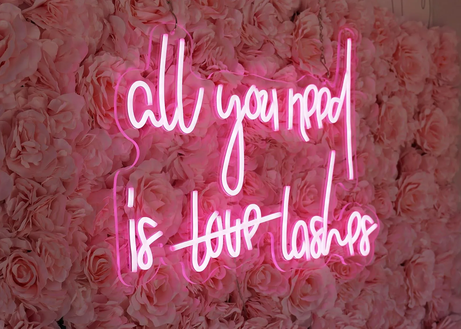 The studio's rose neon sign — 'all you need is lashes' — glowing over the flower wall