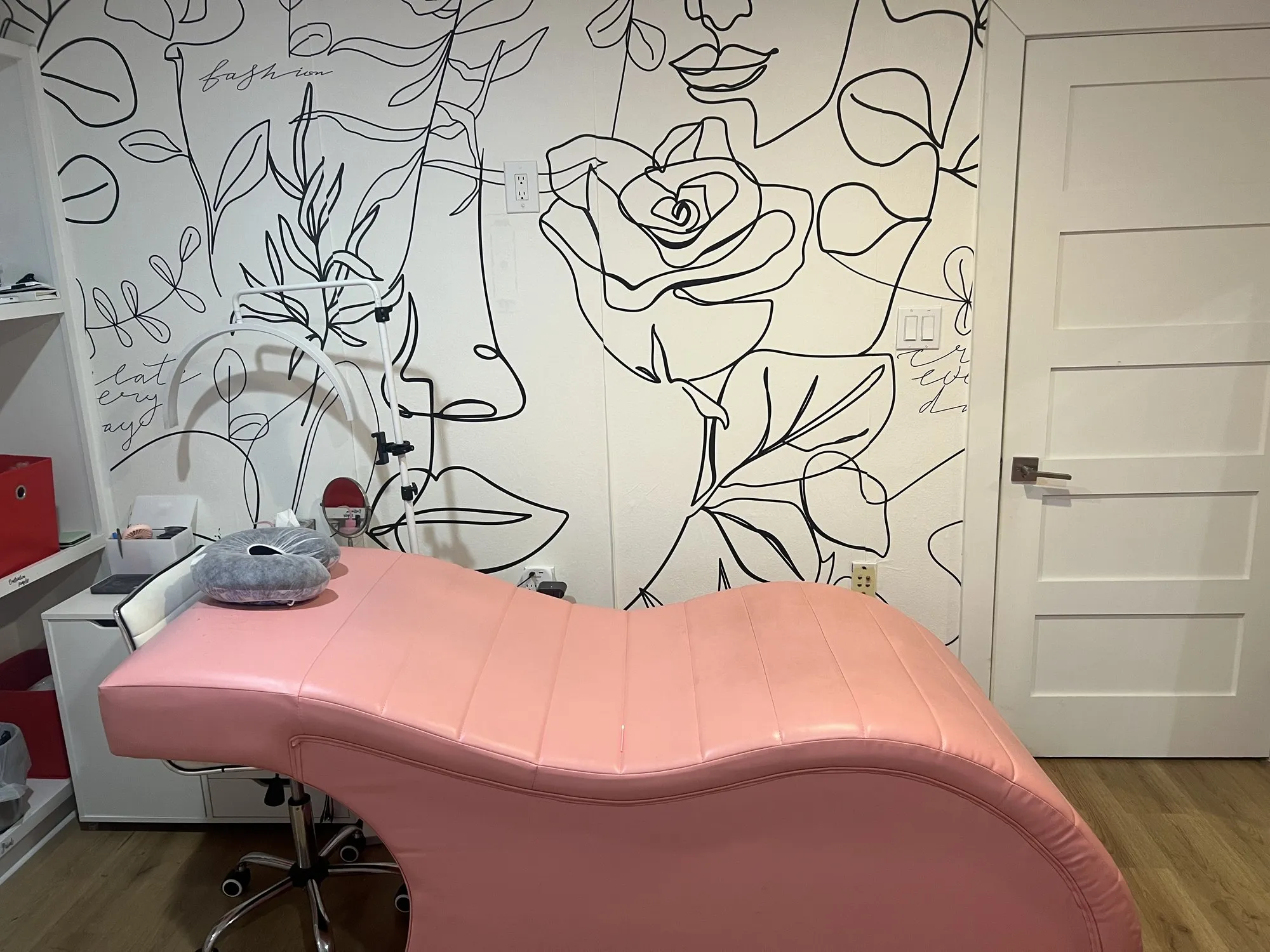 The lash room at Eye Charm — a pink treatment bed against a black line-art floral mural