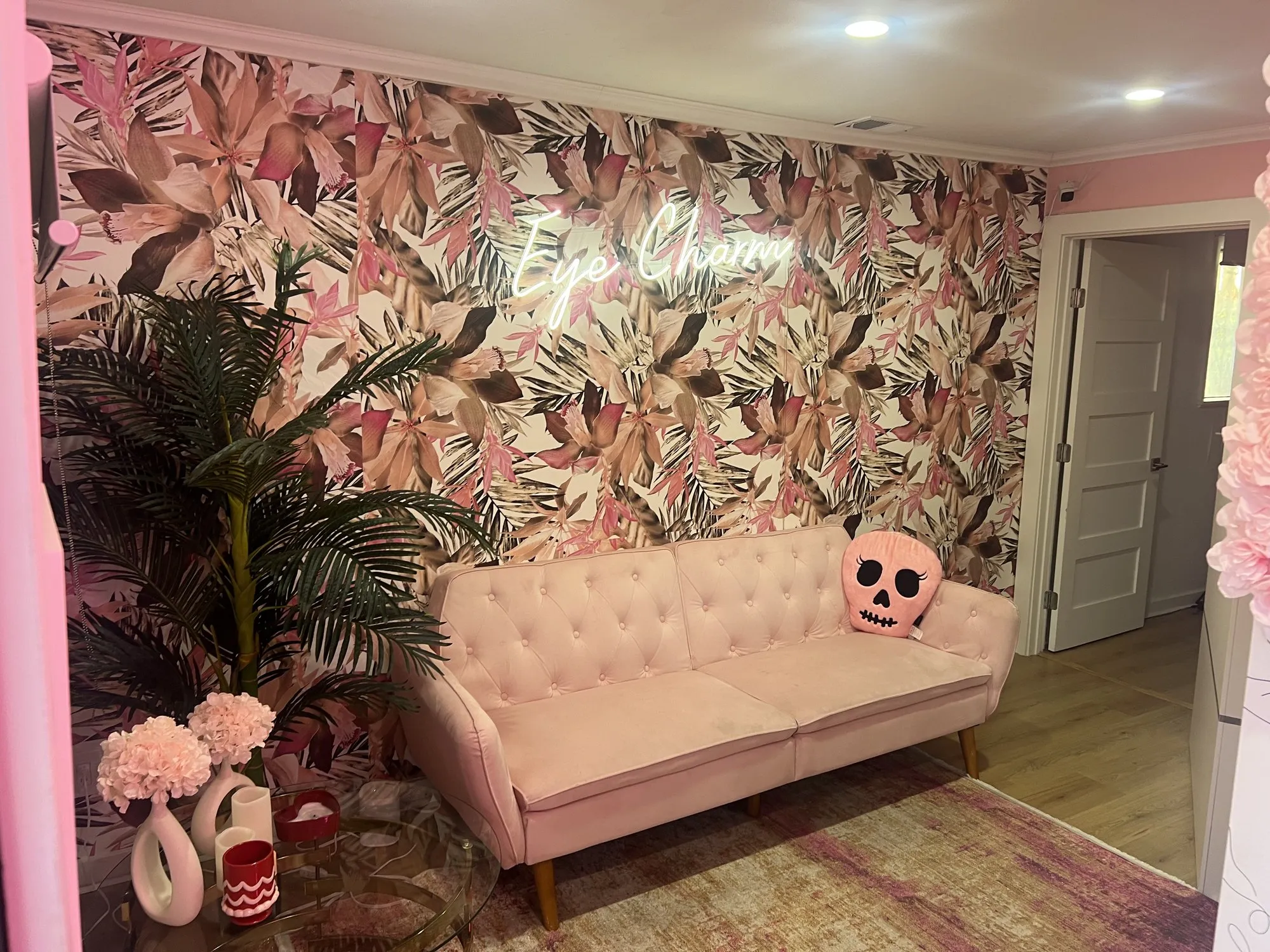 Wide view of the Eye Charm studio lounge with floral wallpaper, palm, and blush sofa